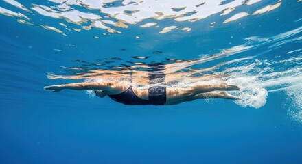 A person swims underwater, captured in a dynamic photo, showcasing athleticism and movement in clear blue water with sunlight filtering through