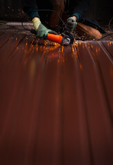 A close-up of a worker wearing gloves cutting a sheet of metal with a grinder, sparks flying. An unrecognizable man at a construction site working with metal structures. vertical banner copy space