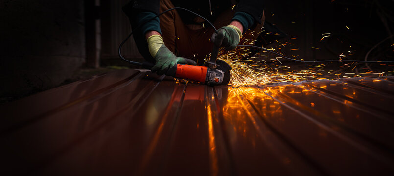 A close-up of a worker wearing gloves cutting a sheet of metal with a grinder, sparks flying. An unrecognizable man at a construction site working with metal structures. banner - Powered by Adobe