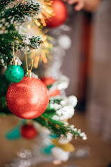 Shiny red and green Christmas tree balls, decorations hanging from dark green branches, create a festive atmosphere.