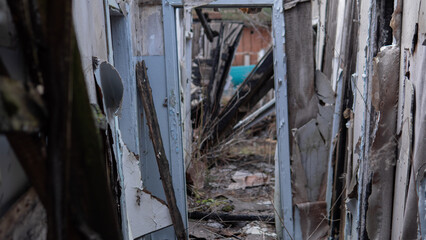 Inside a run-down building, walls are crumbling and debris is scattered. Broken doors lead to empty spaces covered in dust and signs of long-term neglect in an abandoned structure.