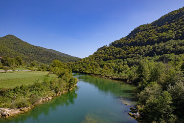 Obraz premium vista panoramica della vallata e dell'ambiente collinare verde attraverso cui scorre il fiume Isonzo, in Slovenia, di giorno, in estate, con cielo sereno
