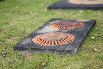 Two orange metal ventilation caps on concrete base for underground septic system or oil interceptor at a gas station service area.