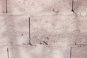 Textured wall of rectangular stone blocks in light beige shades and cement between them.