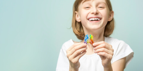 Smiling child holds rainbow orthodontic retainer on pastel background with copy space for dental clinic banner and kids care promotion. © SOLDATOOFF