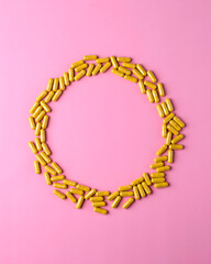 Obraz premium Yellow supplement capsules create circular frame on pink background, clean wellness banner template with central copy space.