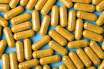 Yellow herbal capsules form dense pattern on blue background, macro texture for vitamin packaging, pharmacy ads, and wellness branding.