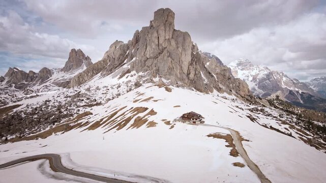 Aerial camera makes a left helix orbit around Ra Gusela peak and rifugio at snowy Passo Giau in the Dolomites, Italy, revealing dramatic alpine scenery.