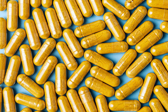 Yellow herbal capsules form bright pattern on pastel blue background for supplement branding, pharmacy ads, health education.