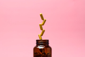 Amber glass supplement bottle on pastel pink background as golden capsules burst out upward, clean wellness banner copy space.