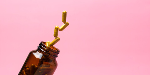 Golden supplement capsules lift from amber bottle on pastel pink background, clean wellness concept with copy space for branding.