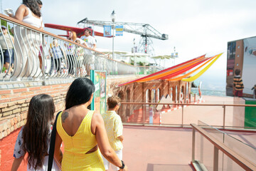A woman in a yellow dress is walking with two children. The scene is lively and cheerful, with people enjoying their time at the beach