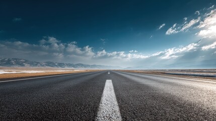 Fototapeta premium Long Straight Asphalt Road with Distant Mountains and Dramatic Sky