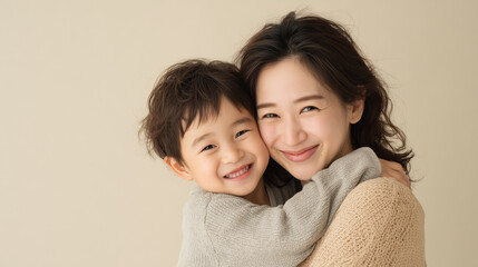 明るいベージュの背景のスタジオで、日本人の母親と幼い息子が寄り添い、正面を向いて微笑んでいるポートレート
