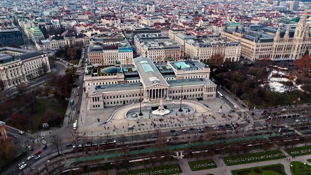 Aerial drone shot panning left over the Austrian Parliament Building, revealing Vienna&rsquo;s cityscape of historic rooftops, broad avenues, and light traffic, captured in clear winter sunlight