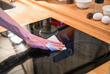 Hand cleaning ceramic cooktop with sponge in modern kitchen