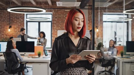 Businesswoman in modern office setting with coworkers in background using digital tablet