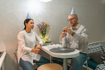 Couple Birthday Celebration Party Apartment: Man pours drink, woman smiles; intimate indoor setting, festive mood.