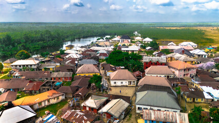 Aerial view of roofs of various colors clustered around the river against a backdrop of dense forest, Soku Community, Port Harcourt, Nigeria.