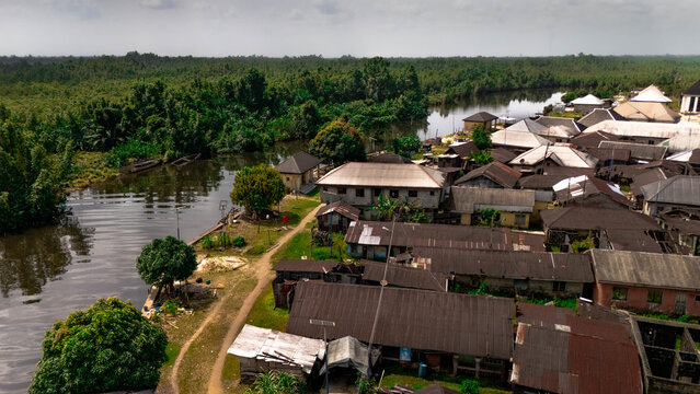 Aerial view of rustic houses nestled alongside a tranquil river, bordered by dense green forest, creating a peaceful contrast of nature and habitation, Abonnema, Port Harcourt, Nigeria.