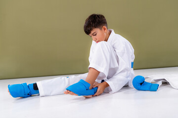 Boy preparing for karate sparring, tightening leg protection equipment showing discipline and technical readiness.