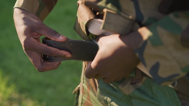 Military Personnel Fastening Equipment Carefully, Uniformed Soldier Tightening Straps In Open Field, Soldier Dressed In Camouflage Outdoors Carefully Fastening His Gear In Prepared Stance