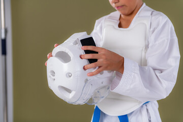 Boy wearing full karate sparring gear putting protective helmet on head before karate session. Highlights safety awareness, control, and disciplined focus.