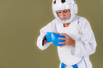 Shotokan karate student in protective gear putting sparring gloves on hands in studio. Highlights safety preparation, discipline, and controlled martial arts focus.
