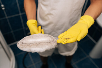 Person wearing protective rubber gloves showing dirty steam cleaner pad and collected dirt, emphasizing effective deep cleaning, hygiene, household chores in bathroom. Concept of domestic work. © dikushin