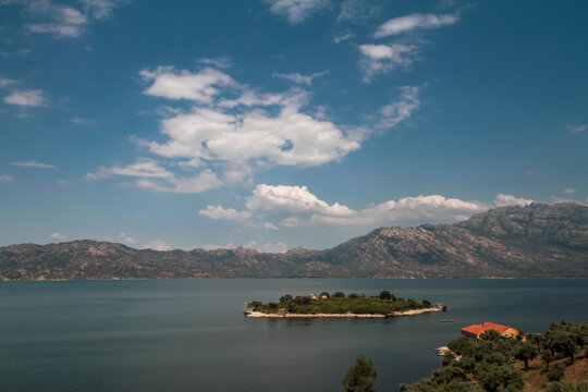 The scenery of Lake Bafa in T&uuml;rkiye's Aegean region includes islands, monasteries, and rock formations, with the Beşparmak Mountains (ancient name: Latmos) in the background.