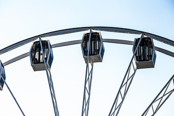 Ferris wheel cabins and metal structure against a clear sky. Amusement park attraction and urban leisure concept.