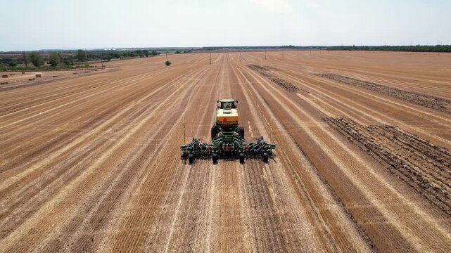 Aerial view of a tractor with planting attachment working the land, creating parallel lines across the vast field, Silistra, Bulgaria.