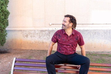 Man with dreadlocks enjoying outdoor leisure, sitting on a bench in a city park