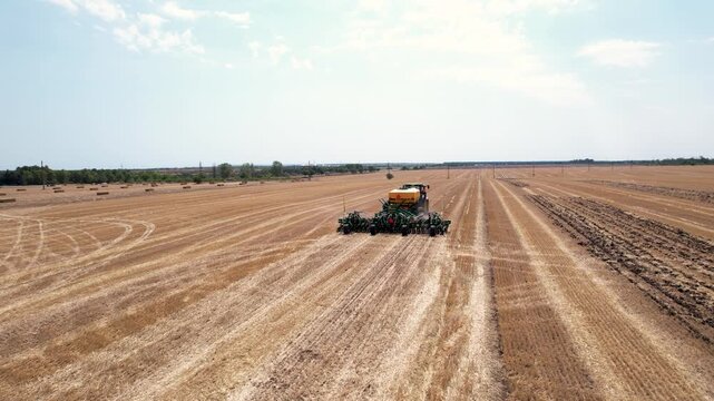 Aerial view of a vast harvested field with a tractor, contrasting golden hues and earthy textures under a clear sky, Silistra, Bulgaria.