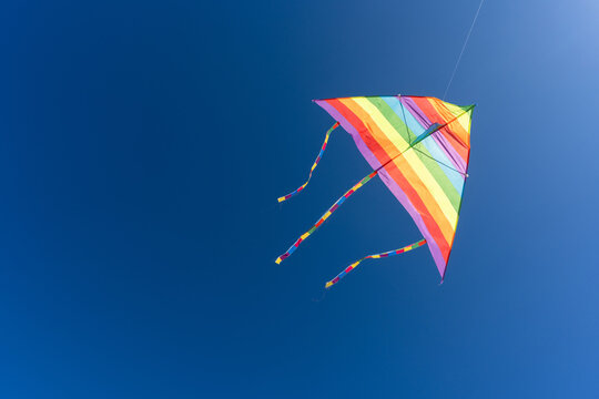 Close-up of a vibrant rainbow kite soaring in the clear blue sky on a sunny day, symbolizing freedom, fun, and childhood joy during a beach adventure