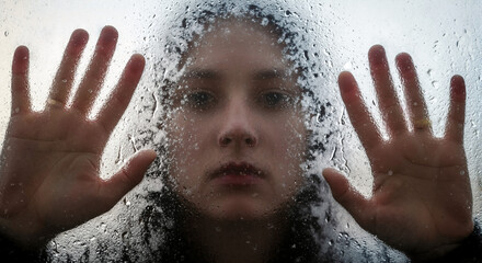 Young woman pressing hands against wet window while looking outside  