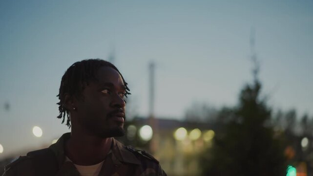 Black ExSoldier Walking Through City Dusk, Camouflage Jacket And Backpack, Blurred Lights And Skyline Behind, Steady Forward Gaze, Cinematic Night Bokeh, Hopeful Return To Civilian Life