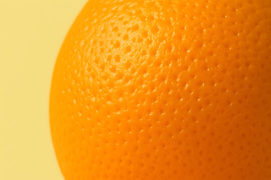 A close-up view of a vibrant orange with a highly textured peel, set against a soft yellow background. The orange's surface is characterized by numerous small pores, giving it a natural and fresh appe