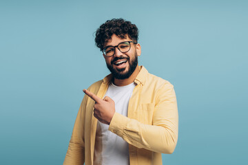Obraz premium Smiling man wearing stylish eyeglasses pointing finger on copy space isolated on blue background