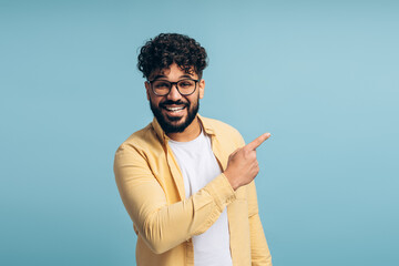 Happy smiling middle eastern man wearing stylish eyeglasses pointing finger showing copy space