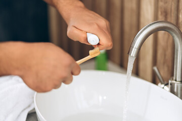 Man preparing to brush teeth with bamboo toothbrush and toothpaste selective focus on hands