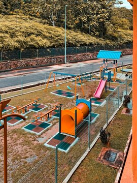 A vibrant outdoor playground featuring a slide, swings, and seesaws set against a lush green forest backdrop.