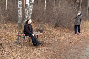 A girl sits on a bench while another woman approaches her in an autumn forest. Mother-daughter relationships, teenage problems, and family disputes.