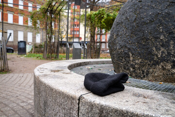 Black knitted hat on the side of a fountain in a city square