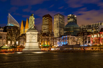 View of William the Silent statue on a pedestal stands prominently against a backdrop of illuminated modern skyscrapers and historic buildings at twilight, The Hague, South Holland, Netherlands.