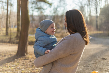 Fototapeta premium Happy family outdoor. Mother embracing her child outdoor. Mom lifting in air little toddler child son. Woman and little baby boy resting walking in park. Mother hugs baby with love care