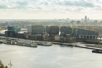Aerial view of the IJ river reflecting the muted sky, with modern buildings lining the waterfront, framed by the city's autumnal hues, Amsterdam, North Holland, Netherlands.