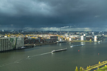 Aerial view of barges glide along the shimmering water, reflecting the steely sky above the cityscape of Amsterdam, North Holland, Netherlands.