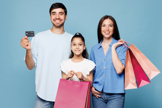 Young happy parents mom dad with child kid daughter girl wear casual clothes holding credit bank card shopping package bags isolated on plain blue background. Family day,Black Friday sale buy concept.