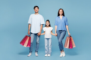 Fototapeta premium Full body young parents mom dad with child kid daughter girl wear casual clothes hold shopping package bags looking camera isolated on plain blue background. Family day,Black Friday sale buy concept.